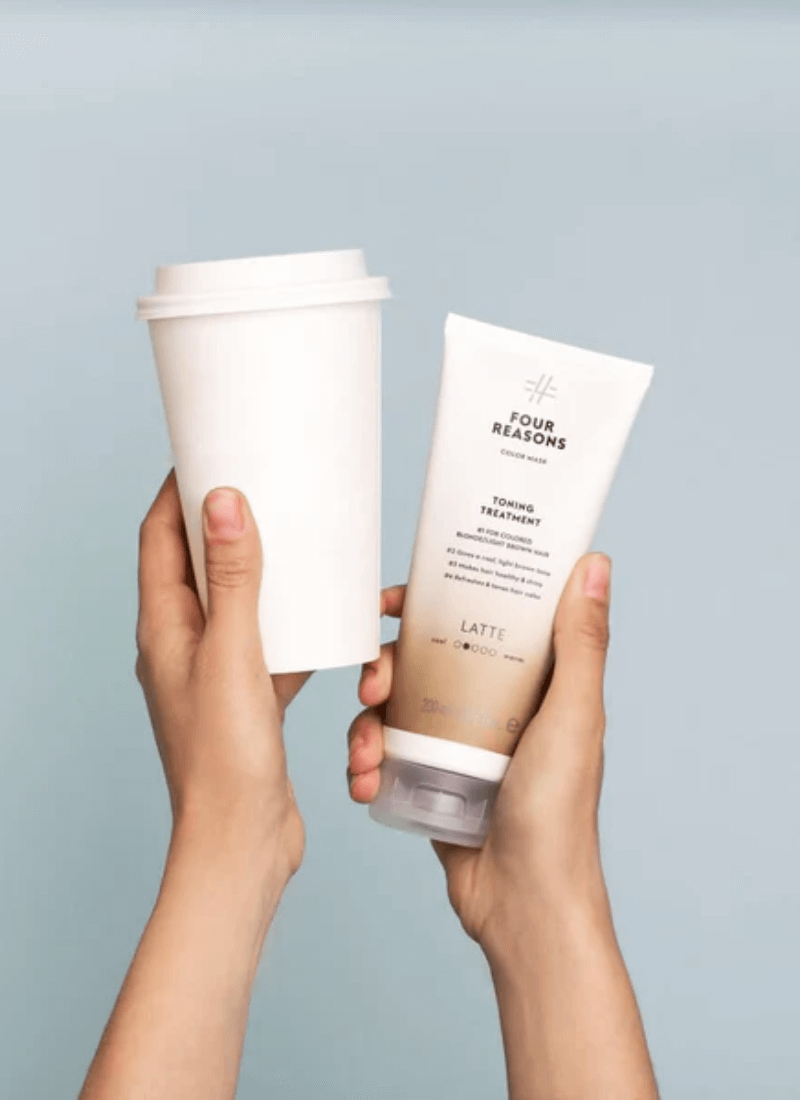 Four Reasons Latte tonizuojanti plaukų kaukė rankose šalia kavos puodelio – kasdienė plaukų priežiūros rutina